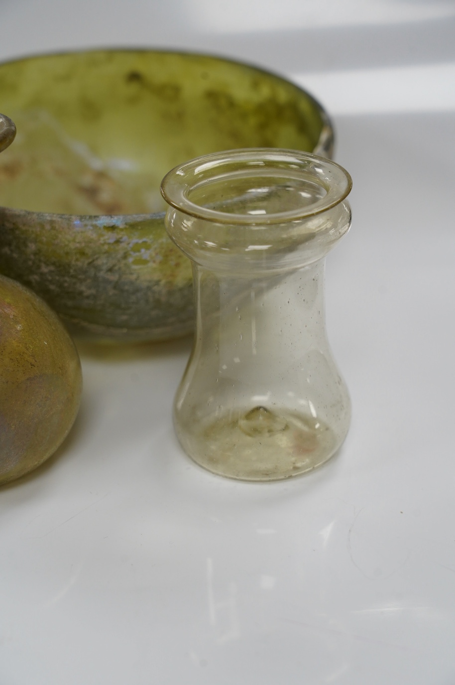 Three items of Roman glassware to include a bowl, a miniature jug and a vessel, bowl 14cm diameter. Condition - bowl repaired